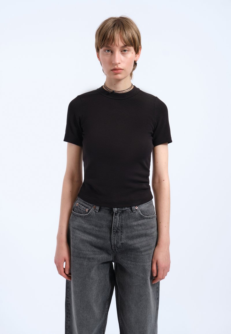 Czarny krótki rękaw dopasowany t-shirt z gładkiego materiału, w połączeniu z luźnymi spodniami dżinsowymi w ciemnoszarym kolorze z wysokim stanem, minimalistyczny design, bez widocznych logo.