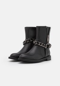 Botas de cuero negras hasta el tobillo con un cierre lateral y un detalle de cadena metálica alrededor del tobillo, con una suela de goma plana.