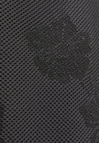 Černá síťovina s vyšívaným květinovým vzorem. Textilie je prodyšná s perforovaným vzorem, což zajišťuje flexibilitu a pohodlí.