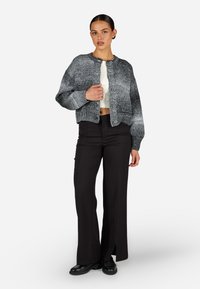 Texturovaný šedý cardigan s kulatým límcem, zapínáním na knoflíky a žebrovanými manžetami, doplněný o elegantní černé kalhoty a černou obuv.