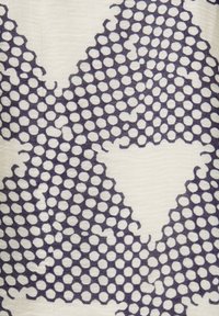 Gros plan d’un motif de pois bleu foncé sur un tissu beige clair avec des formes irrégulières et des amas de points dispersés.