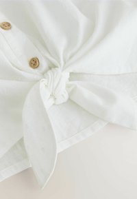 Balts auduma ietinamais ar mezglu centrā, rotāts ar koka pogām un raksturīgu rakstu. Mīksts un viegls materiāls ar gludu virsmu.