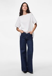 Hvit bomulls-T-skjorte med korte ermer og en avslappet passform, kombinert med mørkeblå vide jeans med femlommers design.