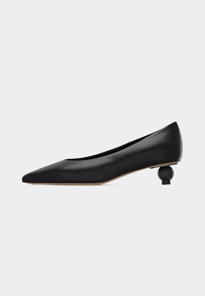 Chaussure noire à bout pointu avec un talon bas unique sculpté en forme ronde et une tige en cuir lisse, vue de profil sur un fond blanc.