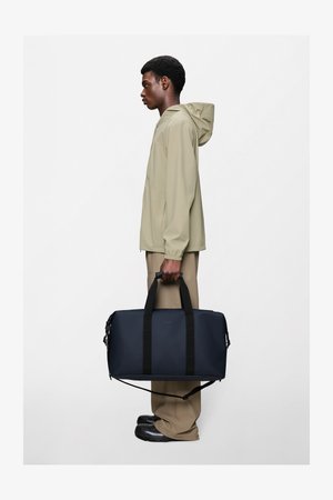 Ciemnoniebieska torba typu duffel z czarnymi paskami, wykonana z gładkiego materiału. Posiada odpinany pasek na ramię oraz zamknięcie na suwak.