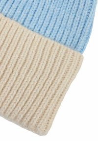 Strickmütze mit einem hellblauen oberen Abschnitt und einem beigen Rippbund. Weiche Wolltextur, deutlicher Farbkontrast und horizontale Rippdetails.
