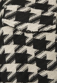 Hahnentrittmuster-Textil in Schwarz und Creme, mit einer strukturierten Webart. Der Stoff zeigt ein markantes, geometrisches Design.
