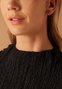 Boucle d'oreille en argent avec un design torsadé, portée à l'oreille. L'arrière-plan présente un tissu noir texturé ressemblant à un matériau froissé.