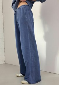 Pantalons large en tissu doux et mélangé en coton. Dotés d'une ceinture à cordon de serrage, de couleur bleue et d'une texture subtile le long des coutures latérales.