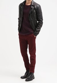 Giacca moto in pelle nera con spalle a coste, maglione lavorato a maglia color porpora e chino bordeaux. Stivali neri con lacci completano il look.