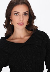 Pulover negru cu tricotaj în este cu o guler gros cu nervuri, având un model texturat și un material moale. Cerceii aurii cu cerc completează ținuta.