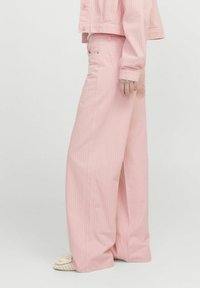 Svijetloružične hlače širokog kroja s suptilnim vertikalnim prugama, izrađene od denima. Imaju džep na struku i opušteni kroj, uparene s teksturiranom obućom.