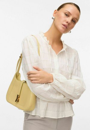 Blouse de couleur crème avec un col volanté et un tissu texturé, associée à un sac à épaule structuré de couleur jaune pâle, mettant en avant un accent en matériel doré.