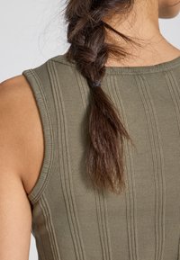 Olive green sleeveless top with ribbed texture and horizontal stripes. The fabric is form-fitting, showcasing a light to medium thickness.