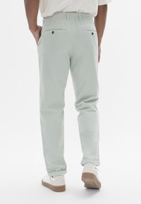 Pantalons en coton vert clair avec une coupe fuselée, poches avant et arrière, et ourlets retroussés, associés à des baskets blanches avec des semelles beiges.