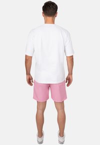 T-shirt bianco in cotone a maniche corte, abbinato a pantaloni corti rosa fino al ginocchio. Sneakers bianche completano l'outfit casual.