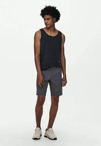 Sort en tanktop, grå shorts og lyse sneakers. Tanktoppen er afslappet, shortsene er knælange med et simpelt design. Neutral farvepalet.