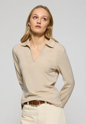 Beige poloshirt met lange mouwen en een V-hals en kraag, met subtiele branding en een zachte textuur, gecombineerd met lichtgekleurde broek en een bruine riem.