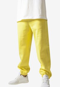 Pantaloni de trening galbeni cu o croială lejeră, manșete elastice și cusături laterale. Asortați cu încălțăminte sport albă pentru un look complet.