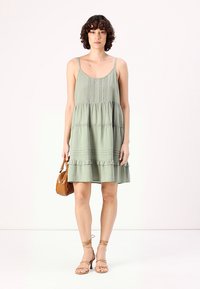 Ανοιχτό πράσινο αμάνικο φόρεμα με στρώσεις ριγέ τελειώματα, υφασμάτινη λεπτομέρεια στο κορσέ, συνδυασμένο με καφέ σανδάλια με λουριά και καφέ τσάντα.