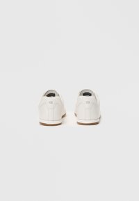Adidași din piele albă, cu un design de tip low-top, textură netedă, talpă din cauciuc de culoare măslinie și detalii subtile ale logo-ului pe călcâi.
