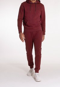 Burgunder hoodie med en framficka och justerbara dragskon, i kombination med matchande joggers, bärs med vita sneakers.