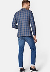 Marynarka w kratę w niebiesko-brązowych odcieniach, dopasowany krój, lekką tkanina, zestawiona z dżinsami w wąskim kroju i czarnymi sneakersami.