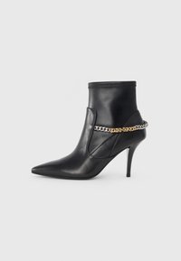 Bottine noire en cuir avec un talon aiguille haut, un bout pointu et une chaîne décorative en or et argent autour de la cheville.
