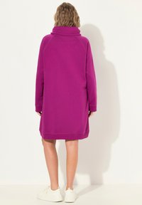 Robe-sweat violette avec un col haut et des manches longues, dotée d'une coupe décontractée et d'un ourlet côtelé, portée avec des baskets blanches.
