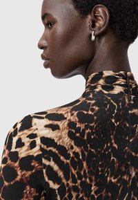 Pardørsværd kjole med høj krave, med brune og sorte mønstre på en tan baggrund. Glat tekstur, tætsiddende design.