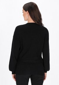 Czarny kardigan z prążkowanej dzianiny, z paskiem w talii, długimi rękawami i miękką teksturą. Charakteryzuje się minimalistycznym wzornictwem bez widocznych wzorów.