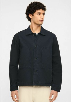 Mørkeblå jakke lavet af bomuld med krave, knaplukning foran og to store påsyede lommer. Glat tekstur med en afslappet pasform.