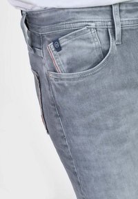 Jeans en denim gris clair avec une coupe slim, cinq poches et de subtils accents de couture rouge sur les côtés. Texture douce avec une finition lisse.