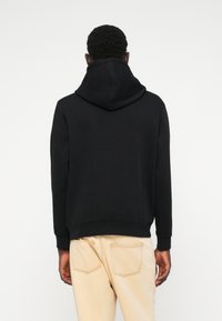 Svart huva tröja med avslappnad passform, med ribbade ärmslut och nederkant. I kombination med ljusa jeans. Enkel design utan mönster.