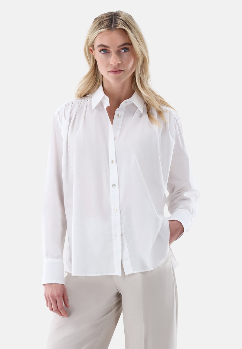 Camicia bianca con bottoni e colletto, caratterizzata da maniche lunghe e una vestibilità morbida. Tessuto liscio con una leggera lucentezza e semplici dettagli con bottoni.