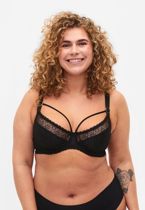 Sort blonde BH med dekorative stropper, en broderet blomsterdesign og bølgede kanter. Justerbare stropper og en hæklelukning er synlige.