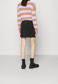 Hnědý a lila pruhovaný chlupatý svetr, černá džínová sukně se zadním zipem, černé kotníkové boty s silnou podrážkou, viditelný texturovaný materiál.