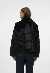 Czarna kurtka z sztucznego futra z kołnierzem, teksturowana powierzchnia i luźny krój. Połączona z ciemnymi dżinsami, podkreślająca współczesną sylwetkę.