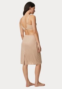 Conjunto de lencería beige que incluye un sujetador sin costuras con tirantes ajustables y una falda hasta la rodilla con una abertura lateral para mayor flexibilidad. Tejido suave y liso.