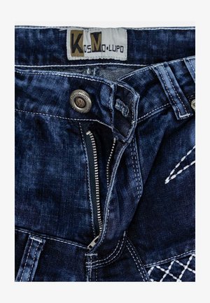 Dunkelblaue Jeans aus Denim mit einer abgenutzten Textur, ausgestattet mit einem Reißverschluss vorne und einem Metallknopfverschluss. Markenlabel an der Taille sichtbar.