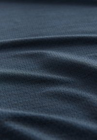 Dunkelblauer Stoff mit glatter Textur, fein und gleichmäßig gerippt und mit dezentem Glanz. Leicht zerknittert, was seinen flexiblen Fall betont.