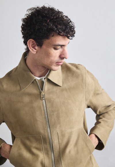 Kreemjookidega nahkjakk, millel on tõmblukk, punktne krae ja kaks esist pockets. Sile tekstuur ja minimalistlik disain. Kuldne riistvara aktsent.