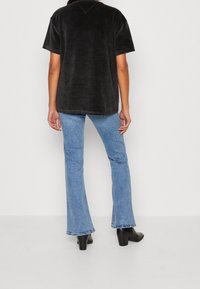 Persona con una blusa negra de manga corta, jeans acampanados de color azul claro y botines negros de tacón, de espaldas a la cámara.