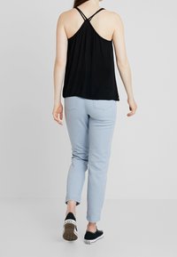 Haut sans manches noir avec des bretelles croisées, associé à un jean skinny bleu clair et des baskets noires décontractées.