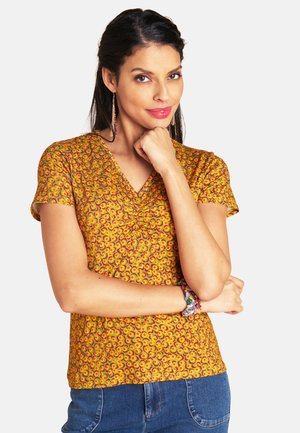 Short-sleeve, yellow blouse with a swirling red and green pattern, featuring a V-neckline and gathered detail at the front.