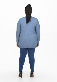 Kék kötött pulóver hosszú ujjakkal, textúrált felülettel és bordás széllel, kék skinny farmernadrággal és magassarkú cipővel párosítva.