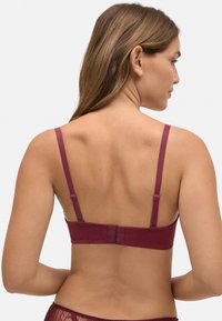 Sostén burdeos con tirantes ajustables, cierre de gancho y ojal, y una textura suave y lisa. La vista trasera destaca un diseño simple y un minimalismo en los detalles.