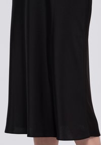 Robe noire longueur genoux avec une silhouette fluide, faite en tissu lisse. Présente un léger éclat et une coupe évasée. Aucune motif ou accent notable.