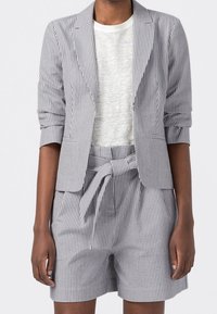 Szary w paski żakiet z podwiniętymi rękawami na jasnoszarym topie, zestawiony z pasującymi szarymi szortami z wysokim stanem w paski, z wiązaniem w talii.