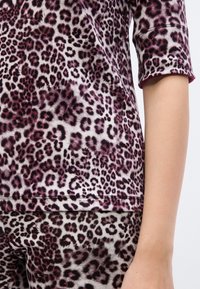 Τοπ με λεοπάρ μοτίβο σε αποχρώσεις του μωβ και μαύρου, με απαλή υφή, κοντά μανίκια και στρογγυλεμένο τελείωμα, σετ με παντελόνι στο ίδιο σχέδιο.